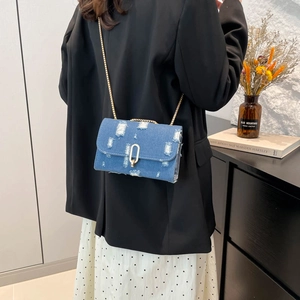 Blue denim crossbody bag with distressed detailing and gold chain strap on model