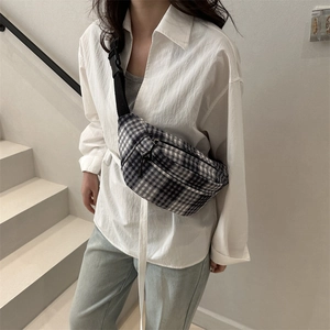 Plaid canvas chest bag with adjustable strap worn by a model in a minimalist setting