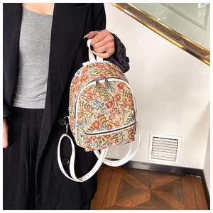 Detailed close-up of a floral tapestry mini backpack with white leather straps and silver zippers
