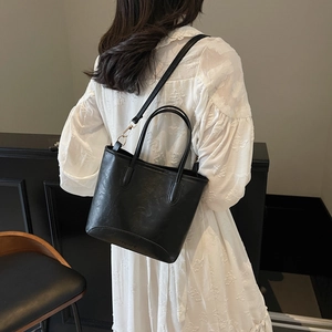 Minimalist black faux leather bucket bag with top handles and adjustable shoulder strap
