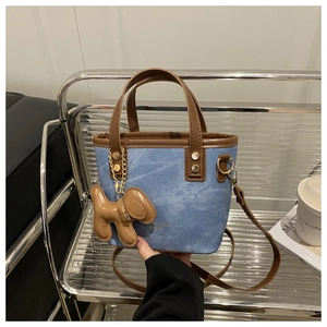 Détail du sac seau en denim bleu avec poignées en cuir marron et pendentif chien