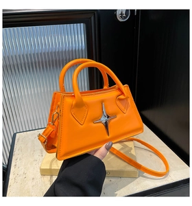 Detail view of bright orange crossbody bag with a silver star hardware on marble surface