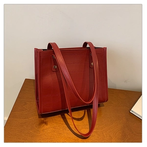 Close-up of deep red crocodile embossed texture and stitching on luxury tote bag