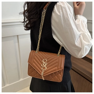 Détail d'un sac bandoulière matelassé marron avec logo SS doré et pompon en métal