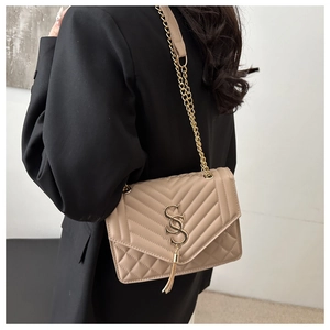 Gros plan d'un sac bandoulière beige matelassé avec chaîne dorée et pompon sur un mannequin