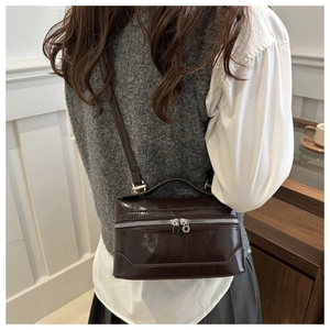 Detail of a chocolate brown patent leather box bag featuring a silver metal zipper close-up