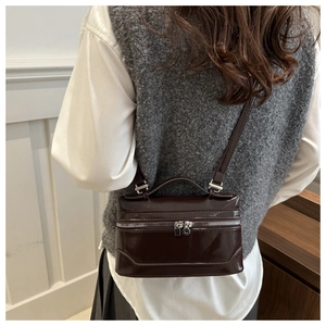 Detail of dark brown glossy box bag with silver hardware and adjustable crossbody strap