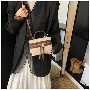Detail of color-block box bag with canvas body, brown leather trim, and long tassels