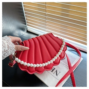 Detailed view of red shell-shaped bag featuring pleated texture and elegant large pearls