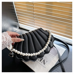 Detail of shell-shaped black leather handbag with pearl handle on vintage newspapers