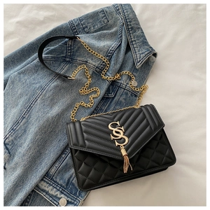 Détail du sac bandoulière matelassé noir avec logo S doré et pendentif à pompon