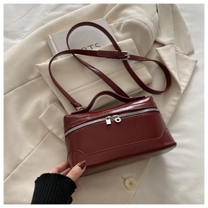 Detailed view of dark red leather semi-cylindrical handbag with smooth finish and gold zipper