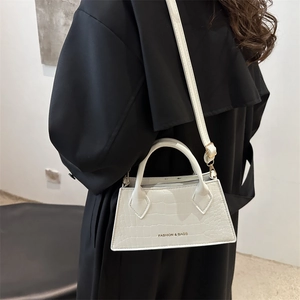 White trapezoid handbag with crocodile texture and gold hardware on black coat