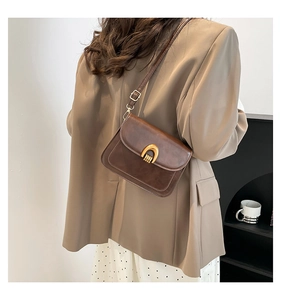 Detailed view of brown leather crossbody saddle bag with a golden U-shaped metal buckle