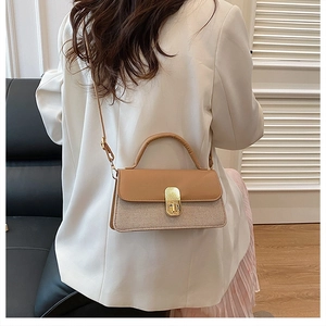 Detail of beige textured fabric and brown leather crossbody bag with gold buckle