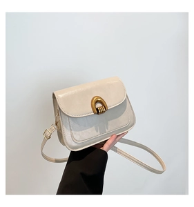 Detail of a cream faux leather crossbody bag with a golden horseshoe buckle held by model