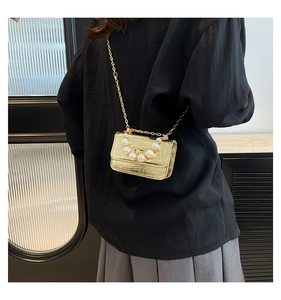 Macro detail of gold crocodile-patterned mini bag with pearl handle and chain strap