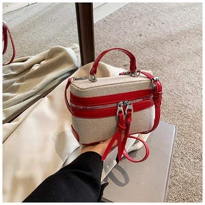 Detail of canvas box bag with red leather trim and dual zipper closure with handle
