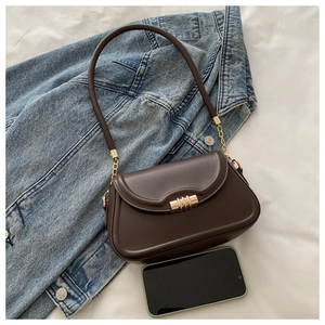 Detailed close-up of dark brown leather underarm bag with gold metal buckle and long strap