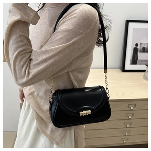 Detail of a black crossbody bag with a gold cylindrical lock and chain strap