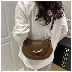 Détail d'un sac selle croissant en cuir marron mat porté par un modèle en intérieur moderne