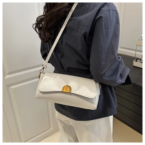 Gros plan d'un sac baguette blanc crème avec fermoir doré porté à l'épaule par un mannequin