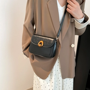 Classic black leather saddle bag with gold U-shaped buckle shown on a female model
