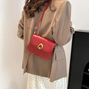 Red faux leather saddle bag with gold horseshoe buckle worn by a woman in a beige blazer