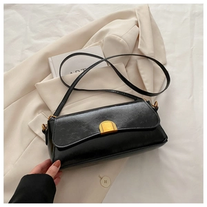 Détail du sac baguette noir en cuir huilé avec une boucle dorée sur un blazer élégant