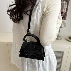 Chic black patent leather hourglass handbag with top handle and slender shoulder strap