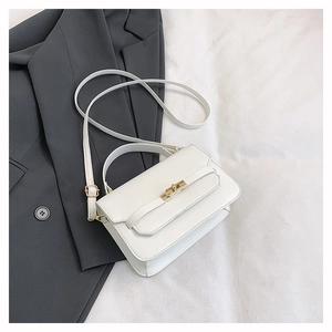 Close-up of a white leather crossbody bag with a golden turn-lock on soft fabric