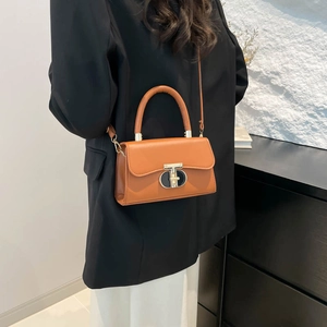 Brown leather crossbody square bag with gold buckle worn over a black blazer jacket