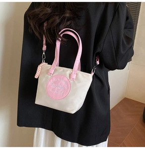 Détail du sac bandoulière crème avec touches roses et texte décoratif sur blazer noir