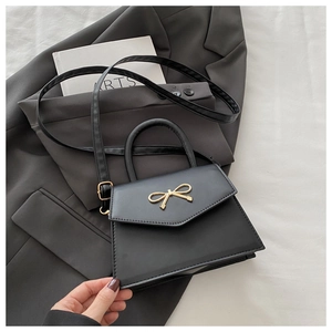 Close-up of black trapezoid handbag with gold bow buckle and leather texture