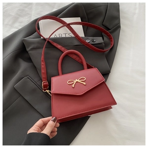 Detail of red faux leather handbag with golden bow metal buckle on a grey blazer background