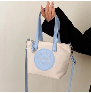 Détail du patch en cuir bleu et de la typographie sur le sac cabas en nylon crème