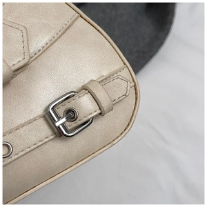 Close-up of beige leather shoulder bag featuring silver metal eyelets and buckle details