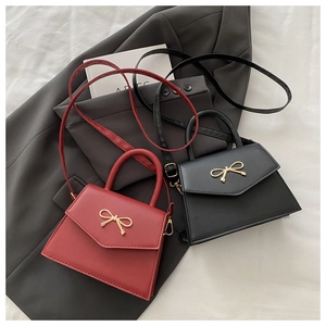 Top view of black and deep red square handbags with gold bow clasps on grey fabric