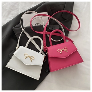 Detail of white and fuchsia mini bags with gold bow clasp on grey fabric background