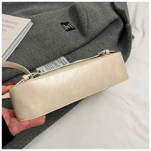Detailed close-up of cream faux leather shoulder bag with silver metal buckles and curved base
