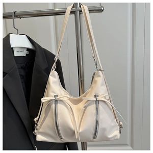 Detail of cream white tote bag featuring decorative zippers and leather bow drawstrings