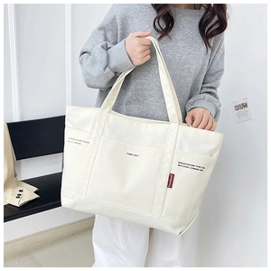 Detail of white canvas tote bag with functional exterior pockets and branded red woven label