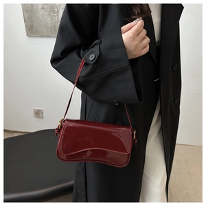 Détail du sac à épaule en cuir verni bordeaux avec base asymétrique et boucle dorée chic