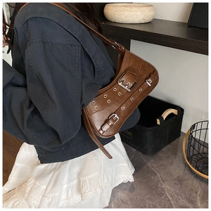 Brown vintage leather shoulder bag with punk rivets and eyelet belt details worn by model