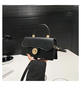Detail of black leather handbag featuring a golden round swivel lock and single top handle