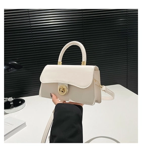 Detail of white leather handbag featuring a golden round swivel lock and metal hardware
