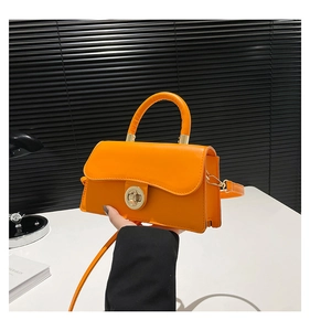 Detail of a bright orange square handbag with a gold twist lock and smooth leather finish