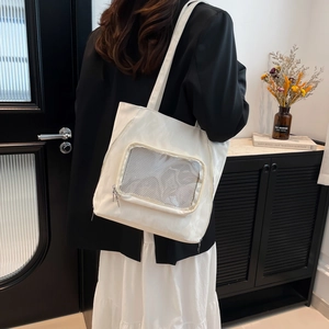 Minimalist white nylon tote bag with mesh pocket shown on shoulder in urban style