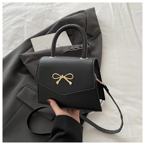 Detail of black trapezoid handbag with gold bow buckle on elegant grey blazer backdrop