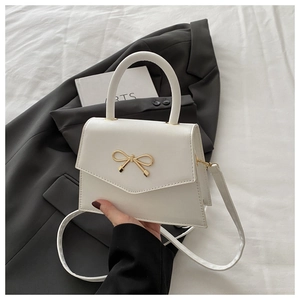 Detail of white PU leather crossbody bag with a golden bow lock and top handle